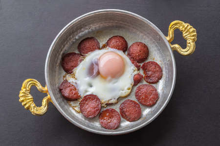 Frying pan with delicious scrambled eggs and turkish sausage on the table