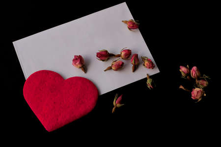 Red hearts, white envelope and small red rose buds on black background . Flat lay, top view. Valentine's day concept.の写真素材