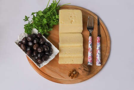 Sliced cheese on a wooden board. Olives, parsley, walnuts.