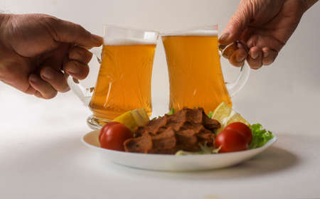 Two friends toasting with beer glasses at the bar. Out of focus meatball plate in the front.の写真素材