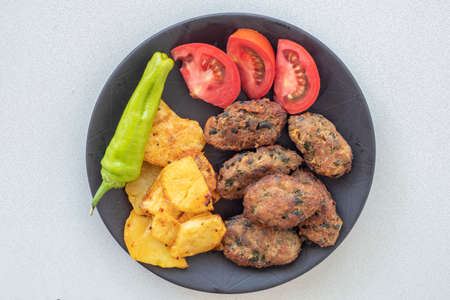 Cyprus meatballs, tomatoes, french fries, peppers. Beautiful presentation on a black plate.