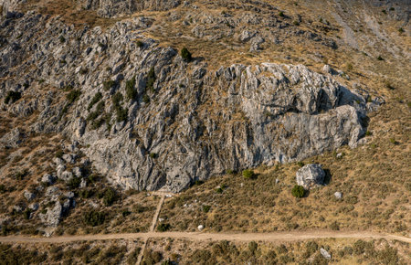 A rocky mountain landscape with a dirt path winding along its base, showing rugged cliff faces and dry terrain.の写真素材