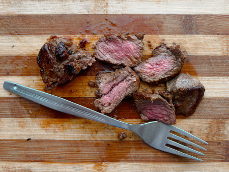Ready to eat a beef steak cut in to slices with a fork on a wooden cutting board.