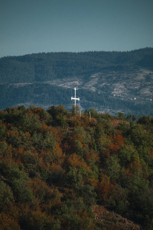A chistian white cross on top of a mountain with another big mountain in the background.の写真素材