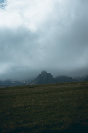 Moody view of a rocky mountain peak covered in fog and clouds with sunlight peeking trough the clouds from above.の写真素材