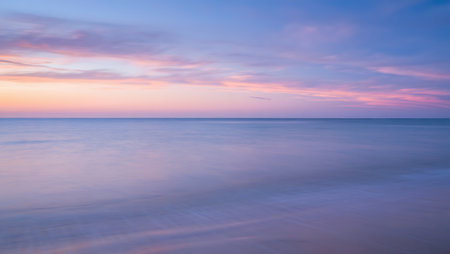 A dreamy coastal scene captures the soft pastels of twilight spreading across the sky and reflecting gently on a serene, smooth shoreline. Shades of pink, lavender, and baby blue streak through the sky and ripple across the wet sands, creating a harmonious blend of color and light. This peaceful moment evokes stillness, clarity, and the quiet beauty of nature.の素材