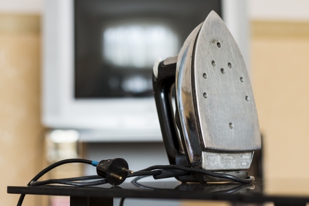 Old iron standing on a glass table in front of the TV in the background. Indoors (at home)の写真素材