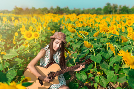 Beautiful girl playing to guitar in field of sunflowers in the morning.の写真素材