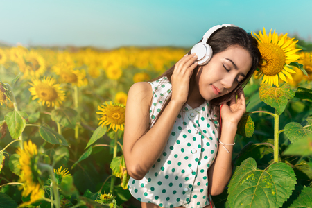 Beautiful girl listening music in field of sunflower in the morning.の写真素材