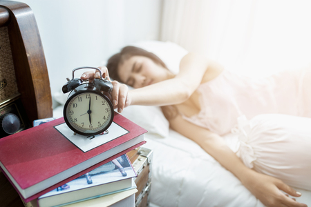 Sleeping asia woman and alarm clock is waking up  at 6.00 AM.の写真素材