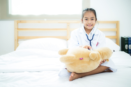 A little doctor girl carrying teddy bear on the bed.の写真素材
