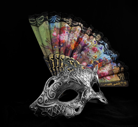 Mask and fan.Silver carnival mask laying with folding fan on black fabric background front viewの写真素材