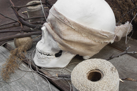 Skull branches with thread skeins. White human skull with cloth, skeins of thread and branches laying on wooden table side view.の写真素材