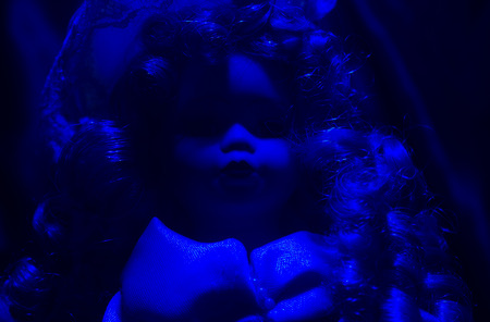 Horror doll blue light front view. Creepy horror photo of a fashioned doll face close up with black background.の写真素材