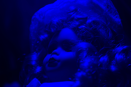 Horror doll blue light angle view. Creepy horror photo of a fashioned doll face close up with black background.の写真素材