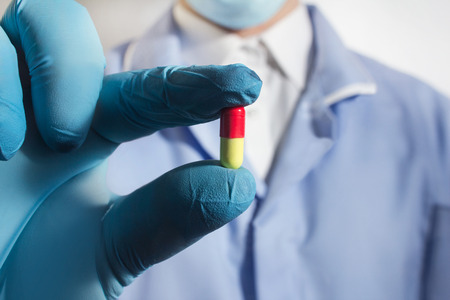 Closeup photo of a fully equipped doctor in rubber gloves holding a pill in one hand.の写真素材