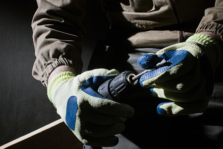 Closeup photo of a worker in outfit with blue gloves inserting a drill in socket on black background with upper light.の写真素材