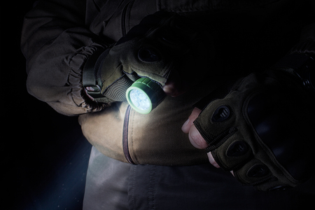 Photo of a male person in brown tactical outfit jacket and gloves using green tactical led flashlight.の写真素材