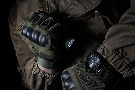 Photo of a male person in brown tactical outfit jacket and gloves using green tactical led flashlight and military watch.の写真素材