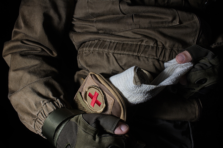 Profile view photo of a male person in brown tactical outfit jacket and gloves holding bangade in first aid kit on black background.の写真素材