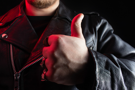 Photo of a biker in black leather jacket with skull rings showing thumbs up on black background.の写真素材