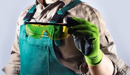 Photo of a worker in green overall outfit with protective gloves holding glasses torso view.の写真素材