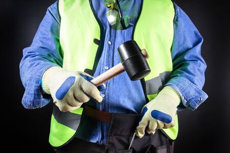 Worker in jeans shirt, green jacket, glasses, tool belt and protective gloves holding a rubber...