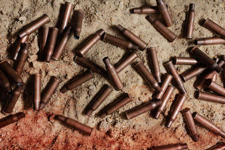 Photo of bloody metal automatic rifle gun shells laying on sand, upper view.
