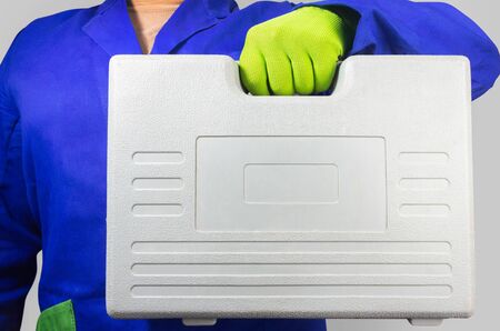 Photo of a worker in blue outfit with gloves holding gray toolcase.