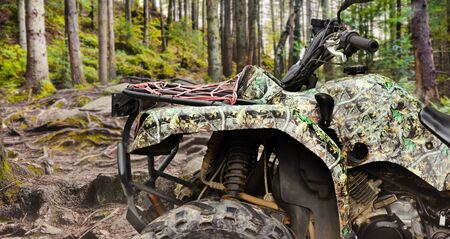 Photo of a camouflaged offroad hunting atv vehicle standing in forest profile close-up view.の写真素材