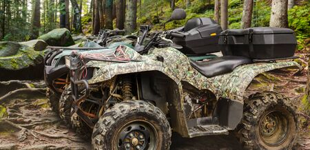 Photo of a camouflaged hunting offroad atv vehicles standing in forest profile  view.