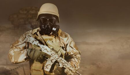Photo of a fully equipped soldier in uniform, armor, helmet and gas mask standing with rifle in...