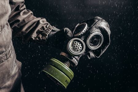 Photo of a stalker  holding soviet gas mask during rain on black background.の写真素材