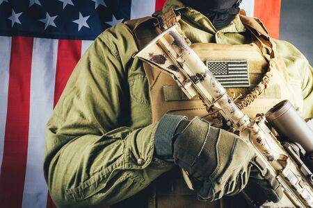 Photo of a fully equipped soldier in tactical armor vest and rifle standing with american flag background.の写真素材