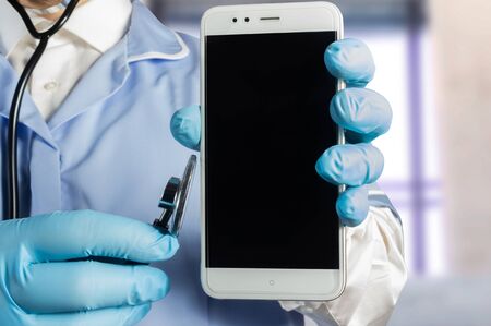 Photo of a doctor in uniform with stethoscope holding a smartphone.の写真素材