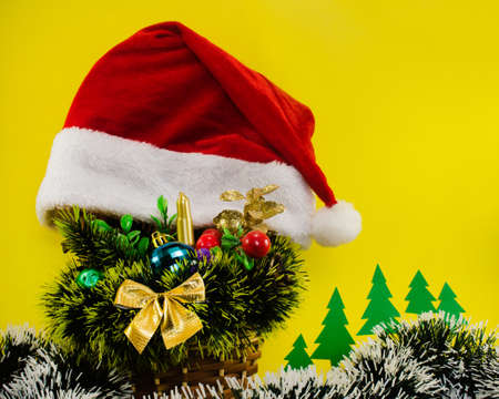 Photo composition of a Christmas bouquet basket with decorative balls, Santa hat and accessories on yellow background.の写真素材