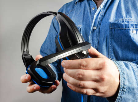 Photo of male hand in shirt holding gaming headphones with microphone closeup view.