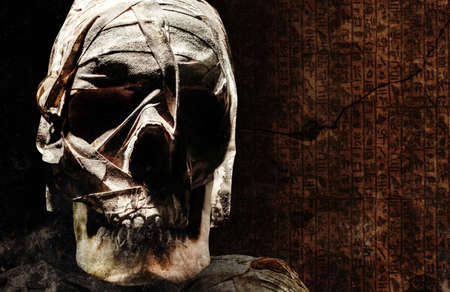 Photo of an old andcient egyptian mummyfied human skull with bondages on dark crypt background.