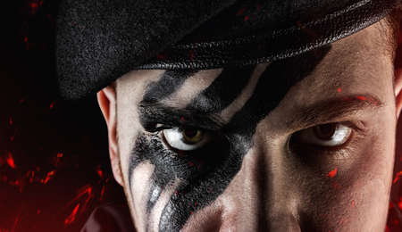 Closeup photo of a painted soldier face in beret on fire ashes black background.の写真素材