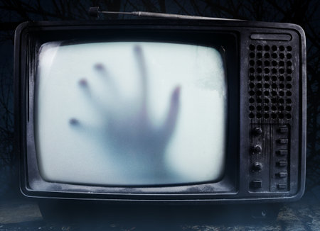 Horror photo of an old black  scary haunted tv set with ghost hand on a screen, standing on dark...