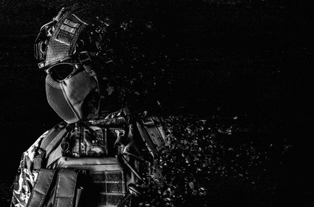 Black and white photo of a fully equipped soldier face and torso standing in tactical clothing and dissolving on grungy black background.の写真素材