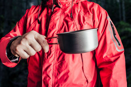 Close-up product photo of hiker man in red travel camping jacket holding metal cup.