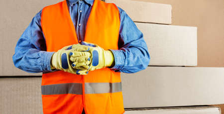 Photo of loader worker in signal vest and protective gloves standing with cardboard boxes.の写真素材