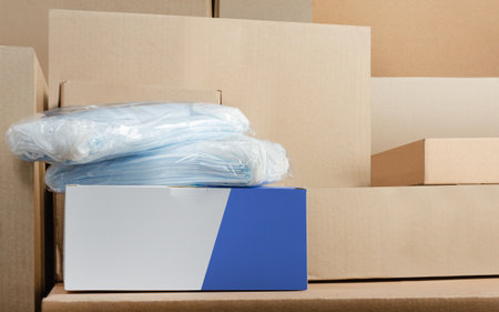 Photo of face medical masks product pack standing on stacked cardboard boxes background.