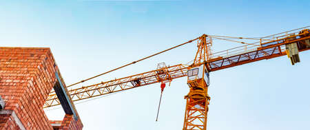 Photo of orange colored building crane on blue sky background and constructon sight.