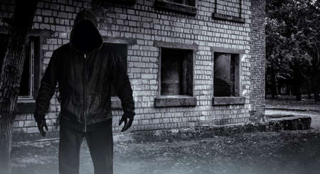 Photo of scary horror stranger stalker man in black hood and clothing on abandoned building background.の写真素材