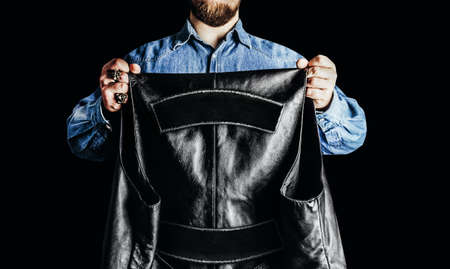Photo of biker man in jeans shirt holding leather vest with patch colors on black background.の写真素材