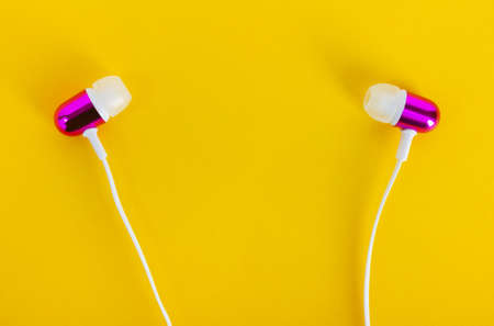 Photo of purple colored wired earphones on yellow backdrop.