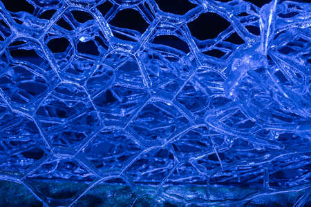 Photo of blue toned frozen metal fence covered in ice on dark background.