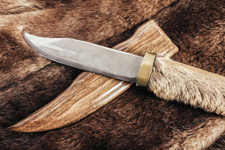 Photo of brown colored animal fur material with hunting knife with shleath laying on it.の写真素材
